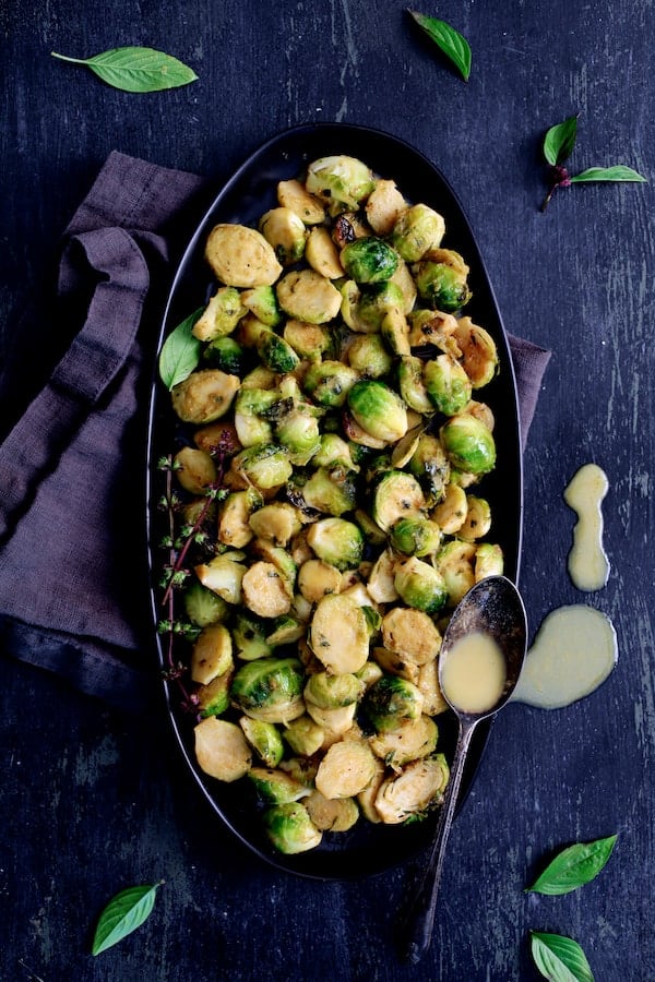 Photo of Roasted Brussels Sprouts with Thai Green Curry Butter on black platter with some of the butter dripped on surface.