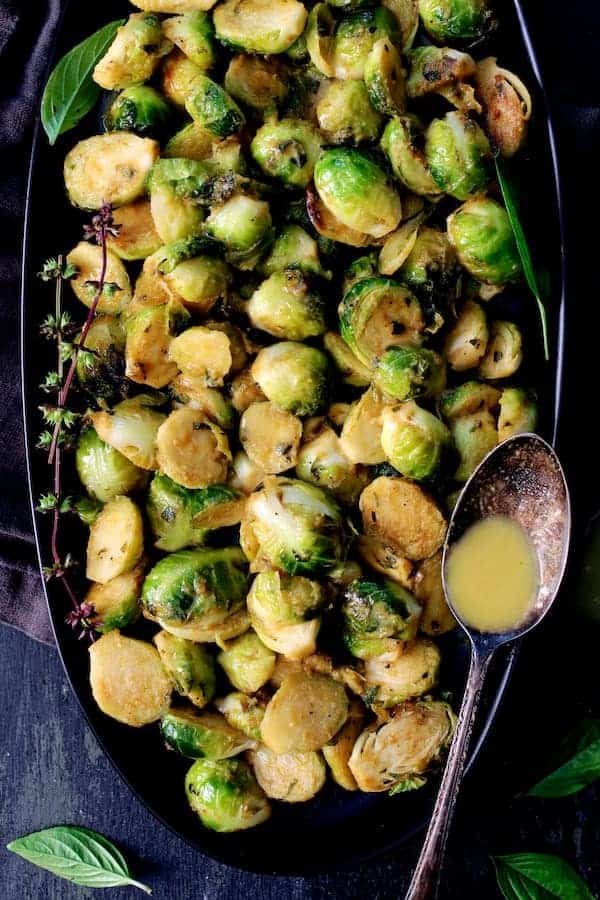 Photo of Roasted Brussels Sprouts with Thai Green Curry Butter with some of the green curry butter in spoon resting on side of the platter.