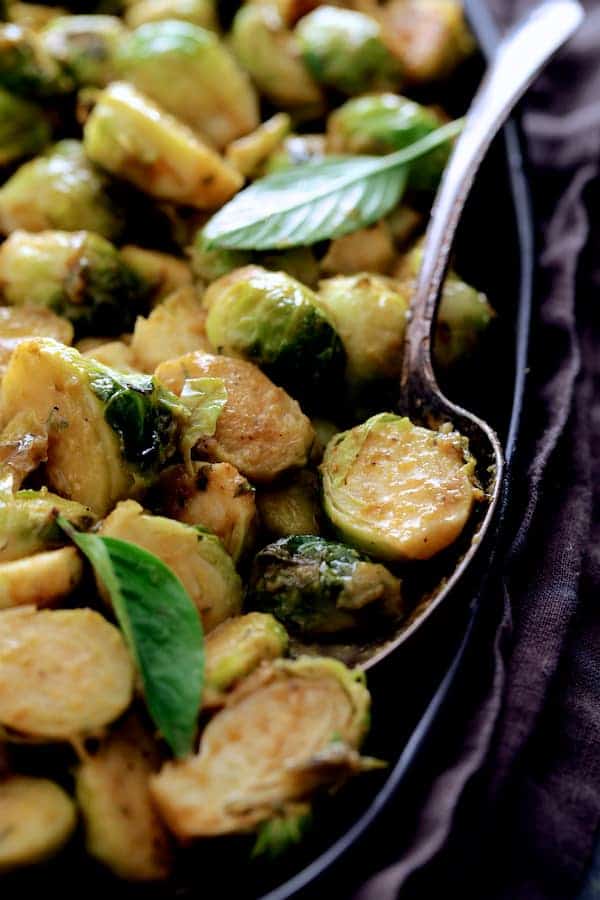 Close-up of Roasted Brussels Sprouts with Thai Green Curry Butter on black platter garnished with Thai basil leaves.