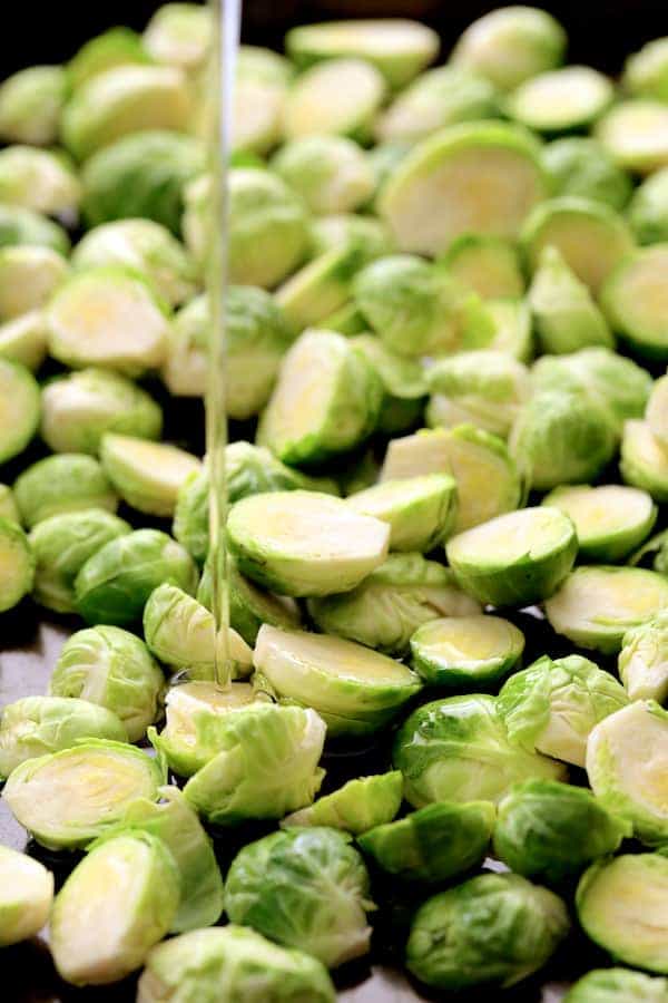 Photo of Brussels sprouts being drizzled with oil before being roasted.
