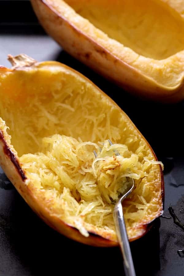Photo of cooked spaghetti squash on baking sheet being shredded with a fork.