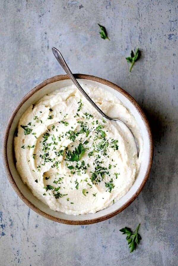 Cauliflower White Bean Puree in earthenware bowl garnished with chopped fresh parsley.