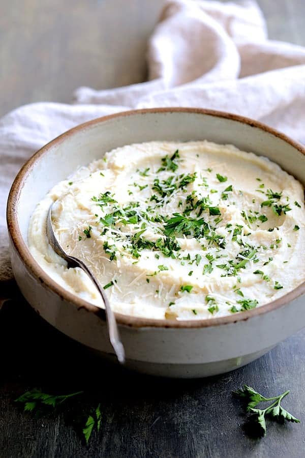 Photo of Cauliflower White Bean Puree in clay bowl garnished with Parmesan cheese and parsley.