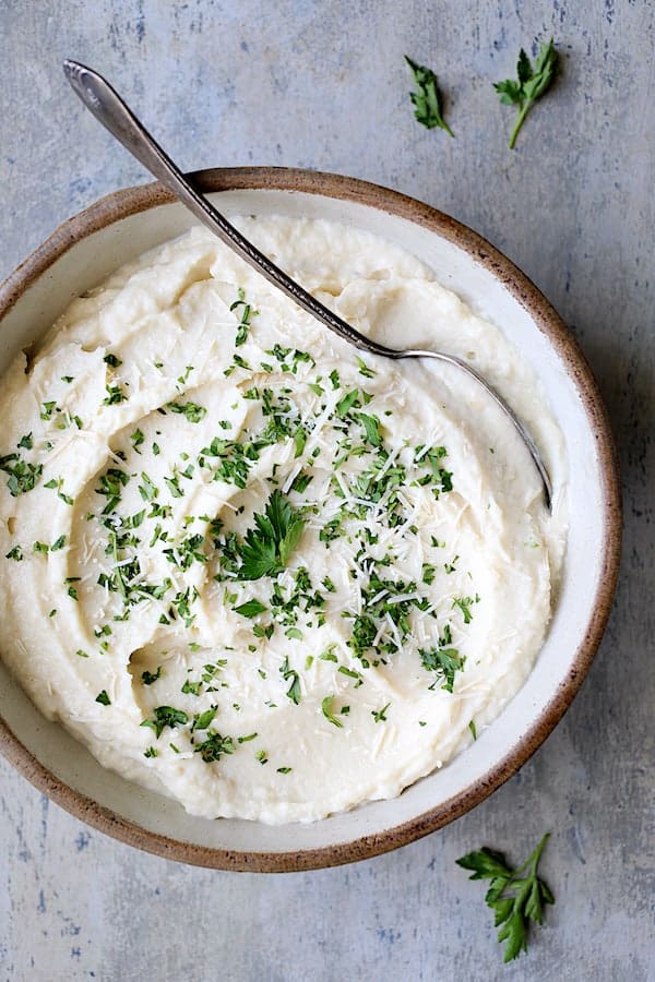 Photo of Cauliflower White Bean Puree in clay bowl garnished with parsley.