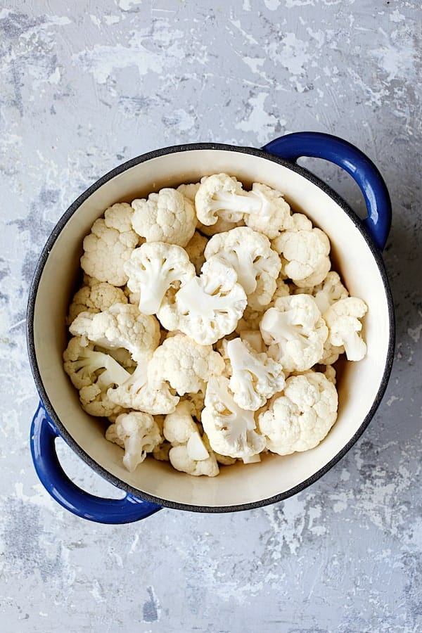 Photo of uncooked cauliflower florets in blue Dutch oven.