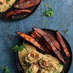Two servings of Spicy Tahini Pork Medallions with Harissa Roasted Sweet Potato Wedges on black plates.