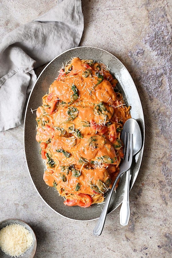 Photo of Chicken in Rosa Sauce with Roasted Red Bell Pepper and Spinach over angel hair pasta on gray-rimmed oval platter.