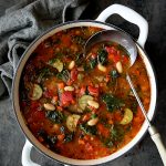 Smoky Spanish Vegetable and White Bean Soup with Kale in white Dutch oven.