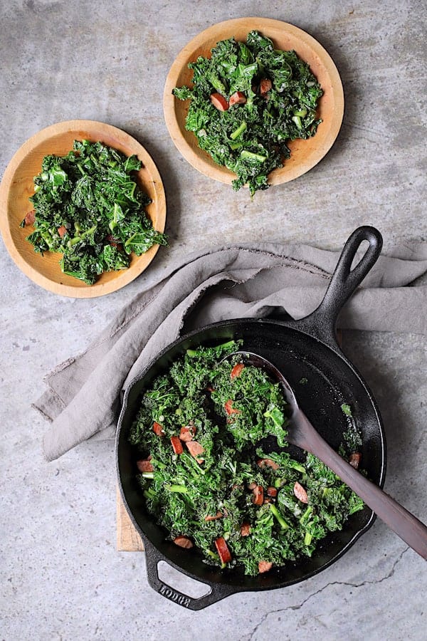 Spicy Sautéed Kale with Andouille Sausage - Overhead shot of dish being served from cast iron skillet onto wooden plates