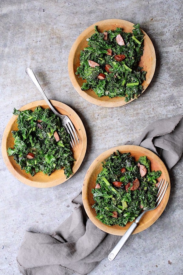Spicy Sautéed Kale with Andouille Sausage - Overhead shot of three small wooden plates filled with this dish on gray background