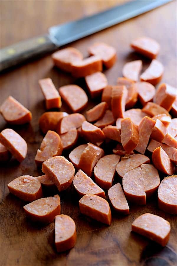 Andouille sausage cut into pieces on wooden cutting board