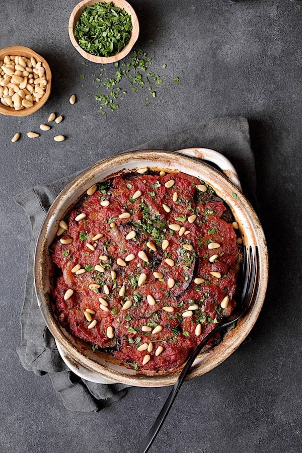 Photo of baked Turkish Eggplant Casserole - Imam Bayildi garnished with pine nuts and chopped parsley.