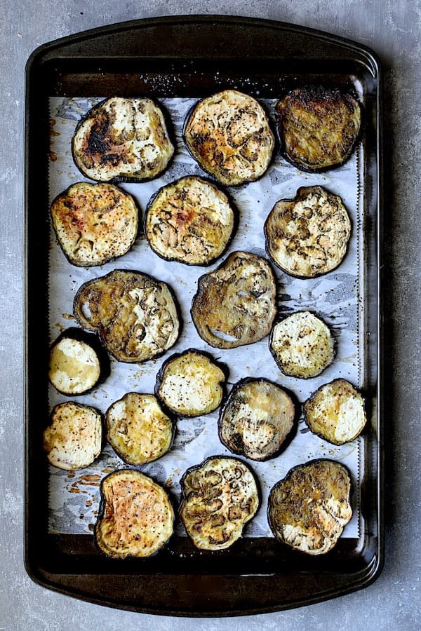 Photo of baked eggplant on parchment paper on baking sheet.