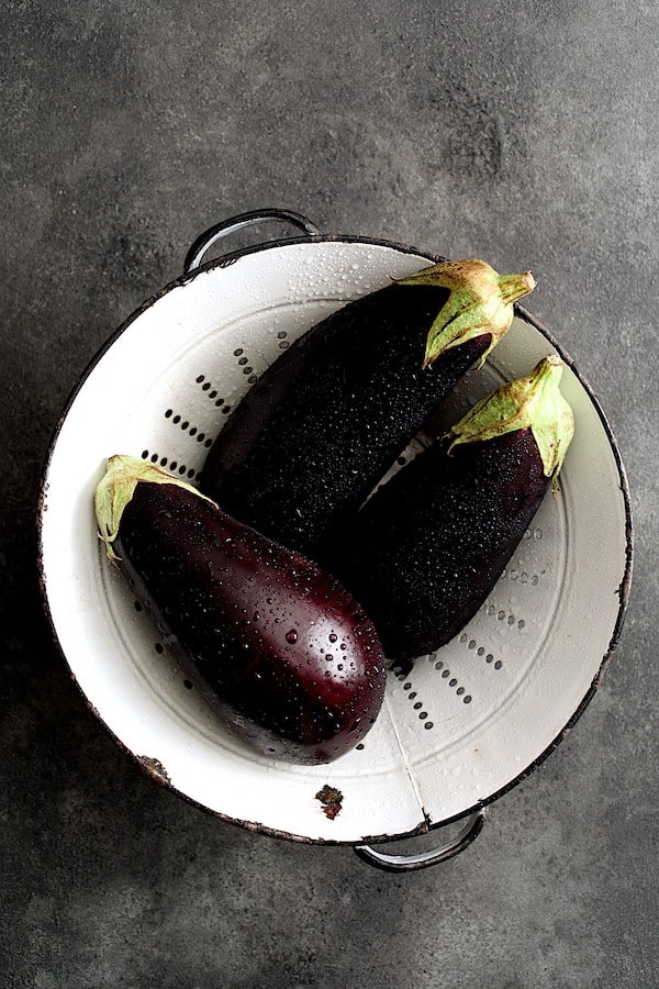 Photo of three freshly washed eggplant in aged white colander.