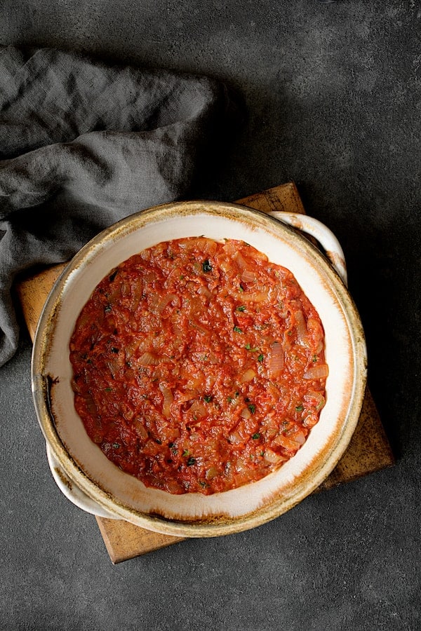 Photo of first layer of tomato sauce in round clay baking dish.