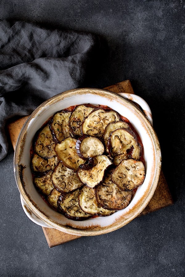 Photo of first layer of eggplant placed over tomato sauce in clay baking dish.