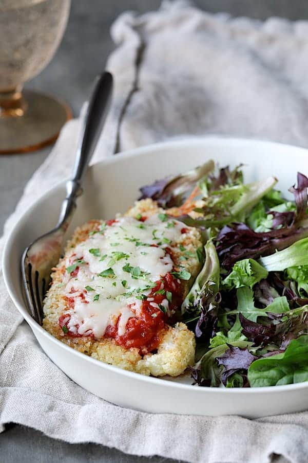 Photo of Cauliflower Parmigiana on white plate with greens.