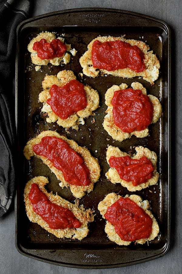 Photo of breaded and baked cauliflower steaks covered with marinara sauce.