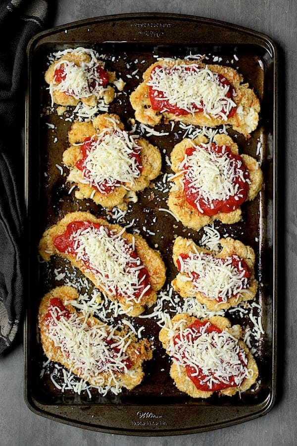 Photo of breaded and baked cauliflower steaks with sauce and sprinkled with cheese.