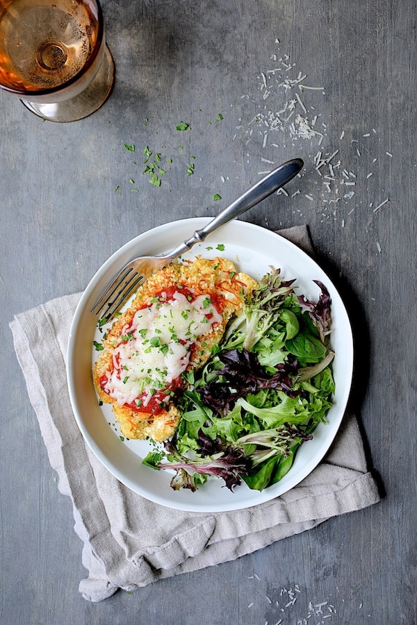 Photo of Cauliflower Parmigiana in white dish on beige napkin on gray background.