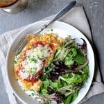 Cauliflower Parmigiana with salad greens on white plate on beige napkin.