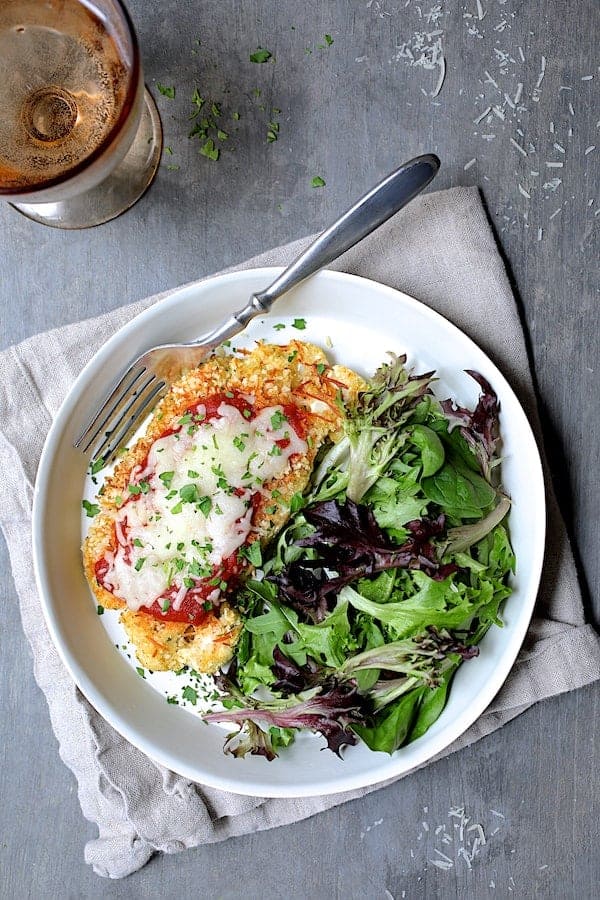 Photo of Cauliflower Parmigiana on white plate with lettuce greens on the side.