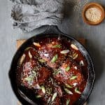 Korean Braised Chicken Thighs in cast iron skillet garnished with scallion and sesame seeds.