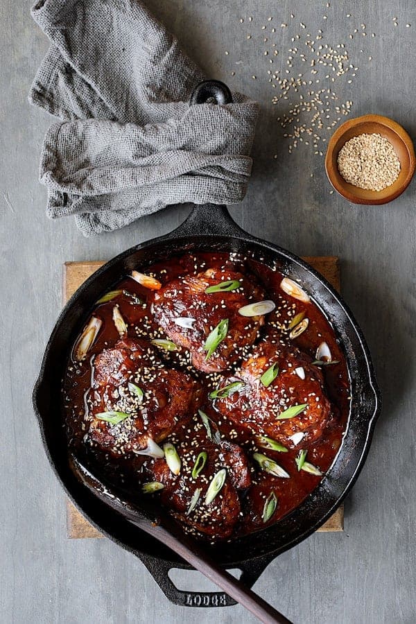 Photo of Korean Braised Chicken Thighs in cast iron skillet garnished with scallion and sesame seeds.