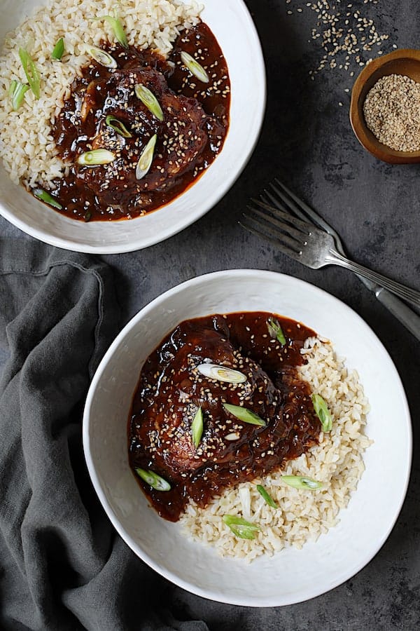 Photo of Korean Braised Chicken Thighs in white bowls with rice garnished with scallion and sesame seeds.