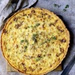 Whole baked Caramelized Onion and Goat Cheese Tart on wood cutting board.