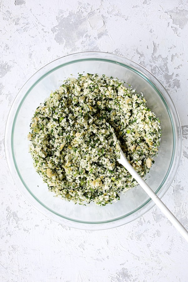 Photo of Cauliflower Artichoke Tabbouleh after ingredients are stirred together with white spoon.