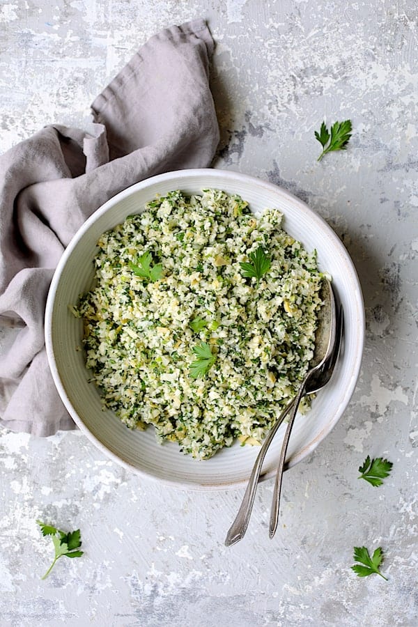 Photo of Cauliflower Artichoke Tabbouleh in white serving bowl garnished with parsley.