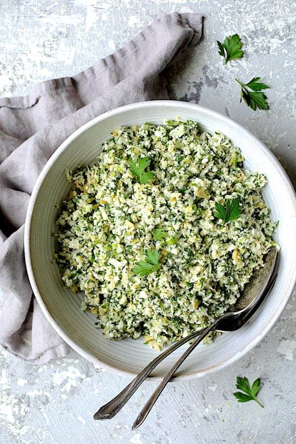 Photo of Cauliflower Artichoke Tabbouleh in white bowl on light gray background with light gray napkin.