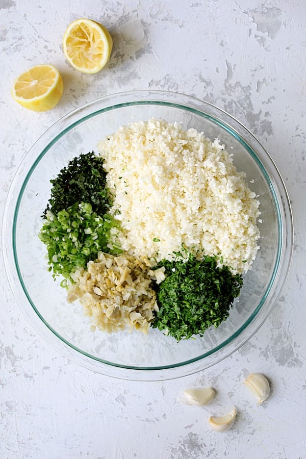 Photo of ingredients for Cauliflower Artichoke Tabbouleh ingredients in glass bowl before being stirred together.