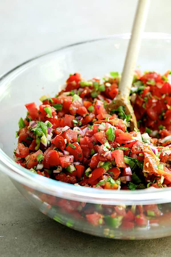 Photo of Salsa Fresca being stirred with wooden spoon in glass bowl.
