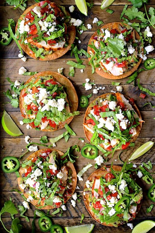Photo of six Chicken Tostadas with Black Bean Guacamole and Salsa Fresca on wooden tray.