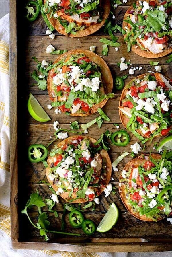 Six Chicken Tostadas with Black Bean Guacamole and Salsa Fresca on wood serving tray.