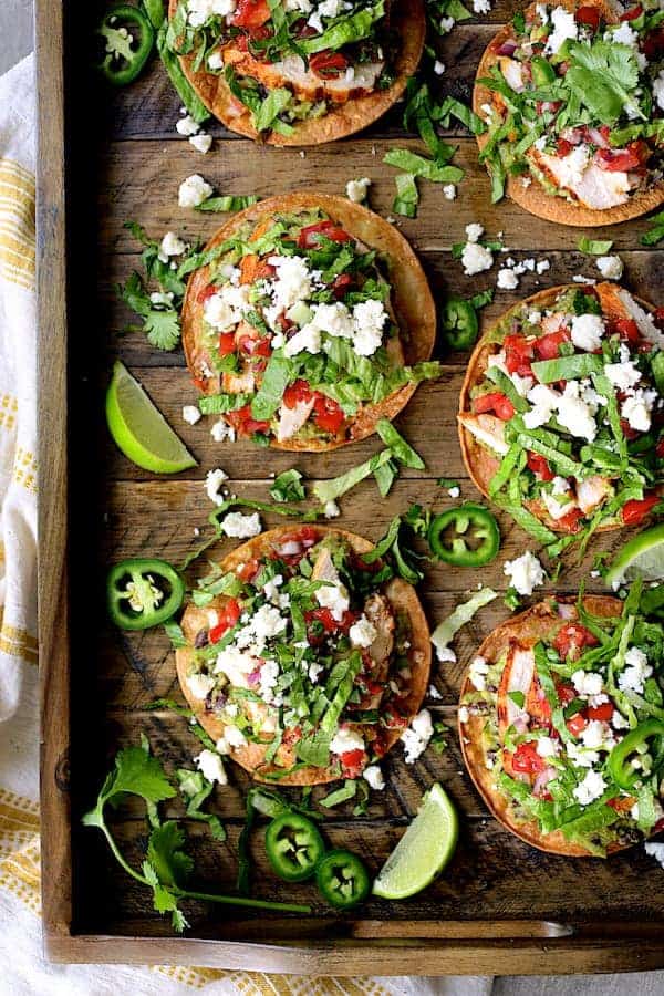 Photo of Chicken Tostadas with Black Bean Guacamole and Salsa Fresca on wooden tray.