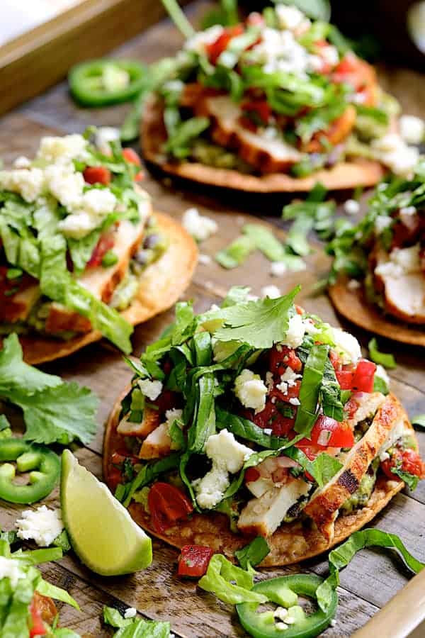 Close-up photo of Chicken Tostadas with Black Bean Guacamole and Salsa Fresca on wooden tray.