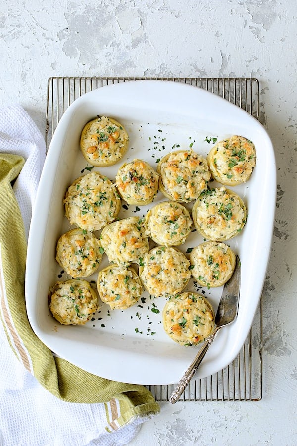 Photo of baked Lemon Parmesan Stuffed Artichoke Bottoms in white baking dish on cooling rack.
