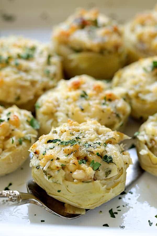 Close-up photo of a Lemon Parmesan Stuffed Artichoke Bottom being lifted out of baking dish with server.
