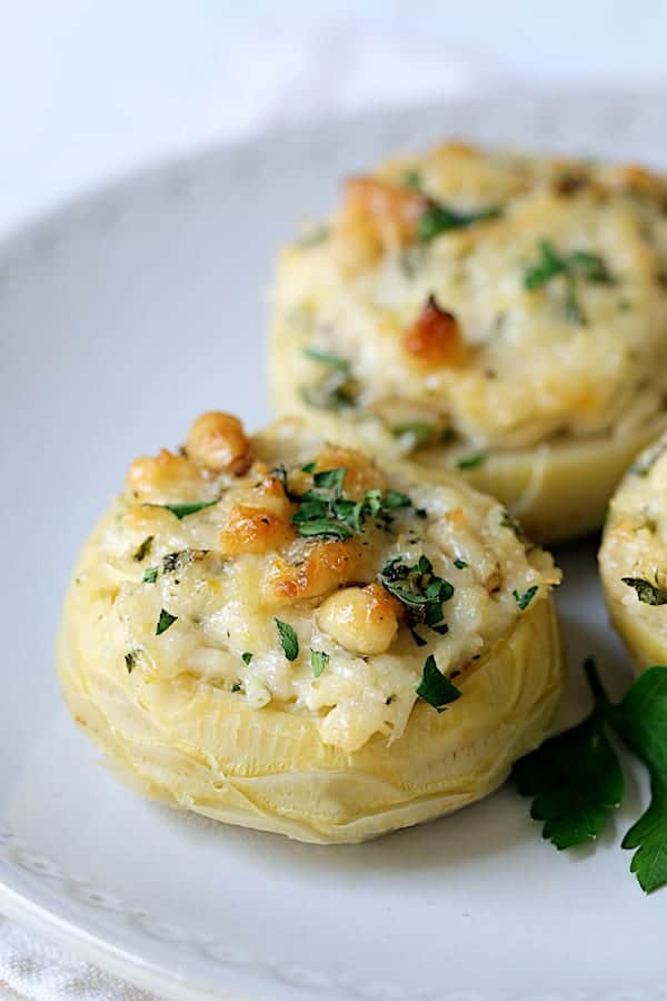 Close-up photo of one Lemon Parmesan Stuffed Artichoke Bottom on white plate.