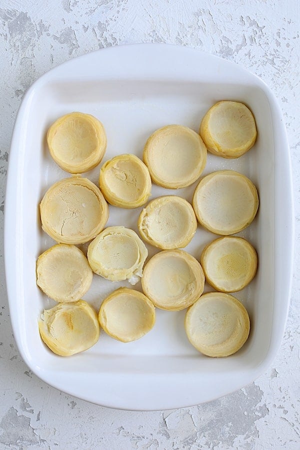 Photo of fourteen empty artichoke bottoms in white baking dish.