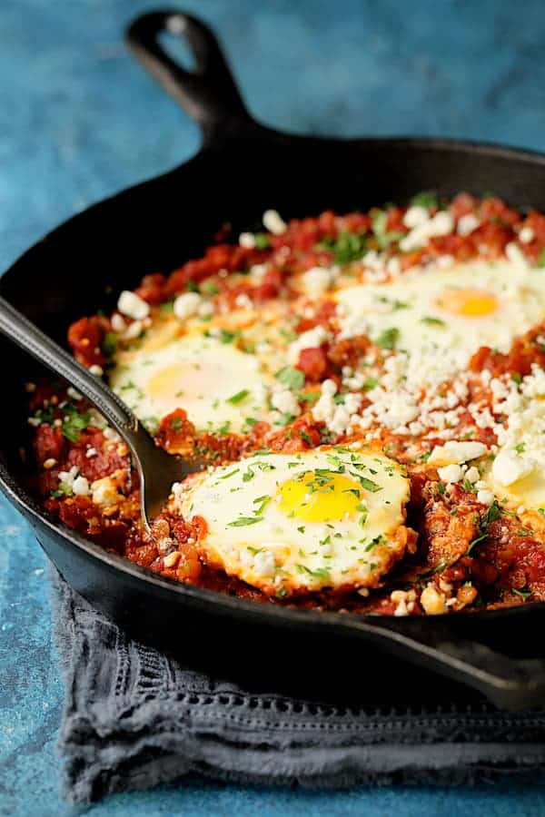 Photo of one of the eggs from the shakshuka being lifted out of skillet with spoon.
