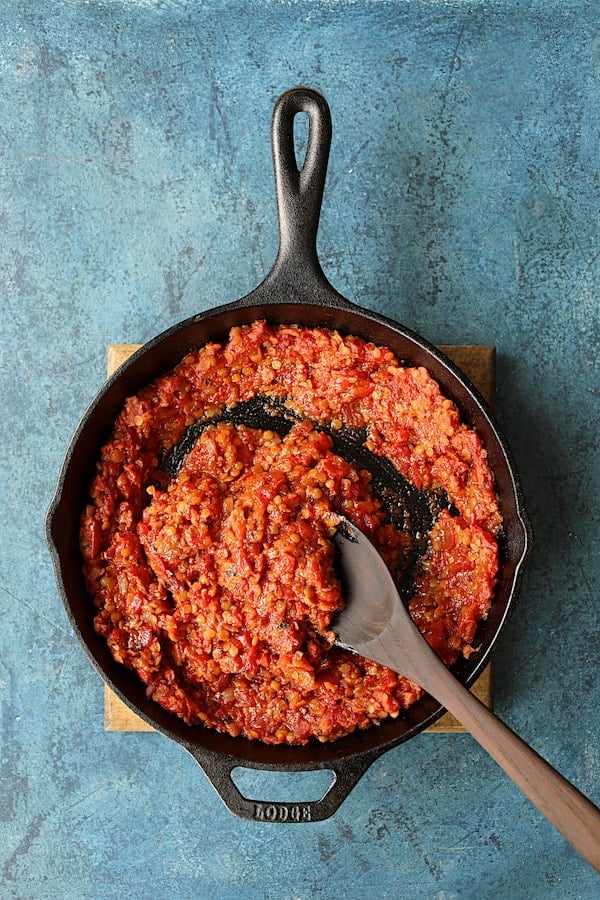 Photo of cooked lentils in tomato sauce being stirred with wooden spoon.