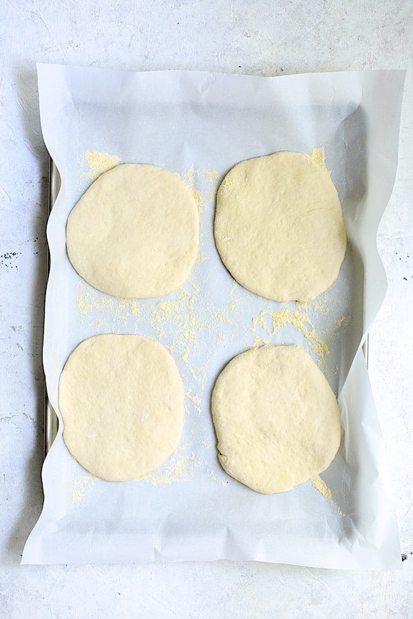 Photo of focaccia dough divided into four individual circles on parchment paper.