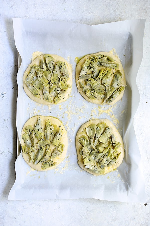 Photo of individual focaccia loaves with artichoke mixture placed on top.