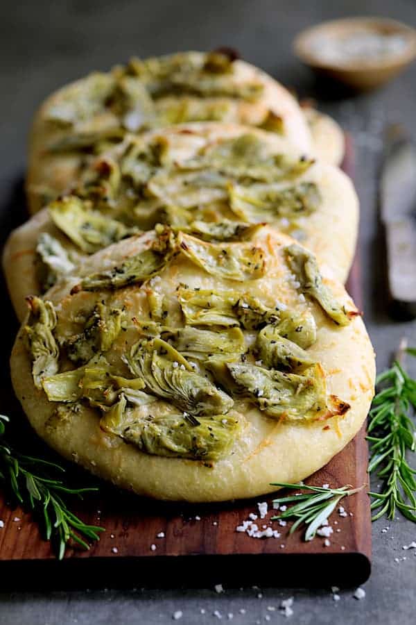 Photo of Artichoke Focaccia with Rosemary on wooden breadboard.