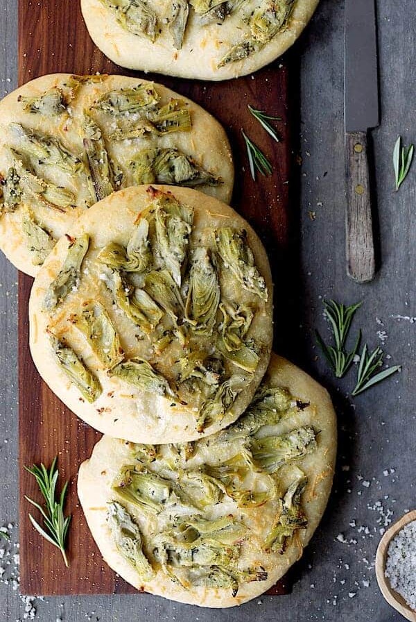 Four Artichoke Foccacia with Rosemary on wood cutting board.