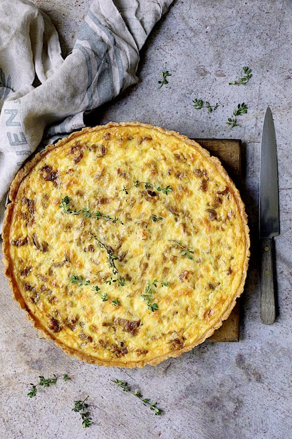 Photo of whole Caramelized Onion and Goat Cheese Tart on gray background garnished with fresh thyme.